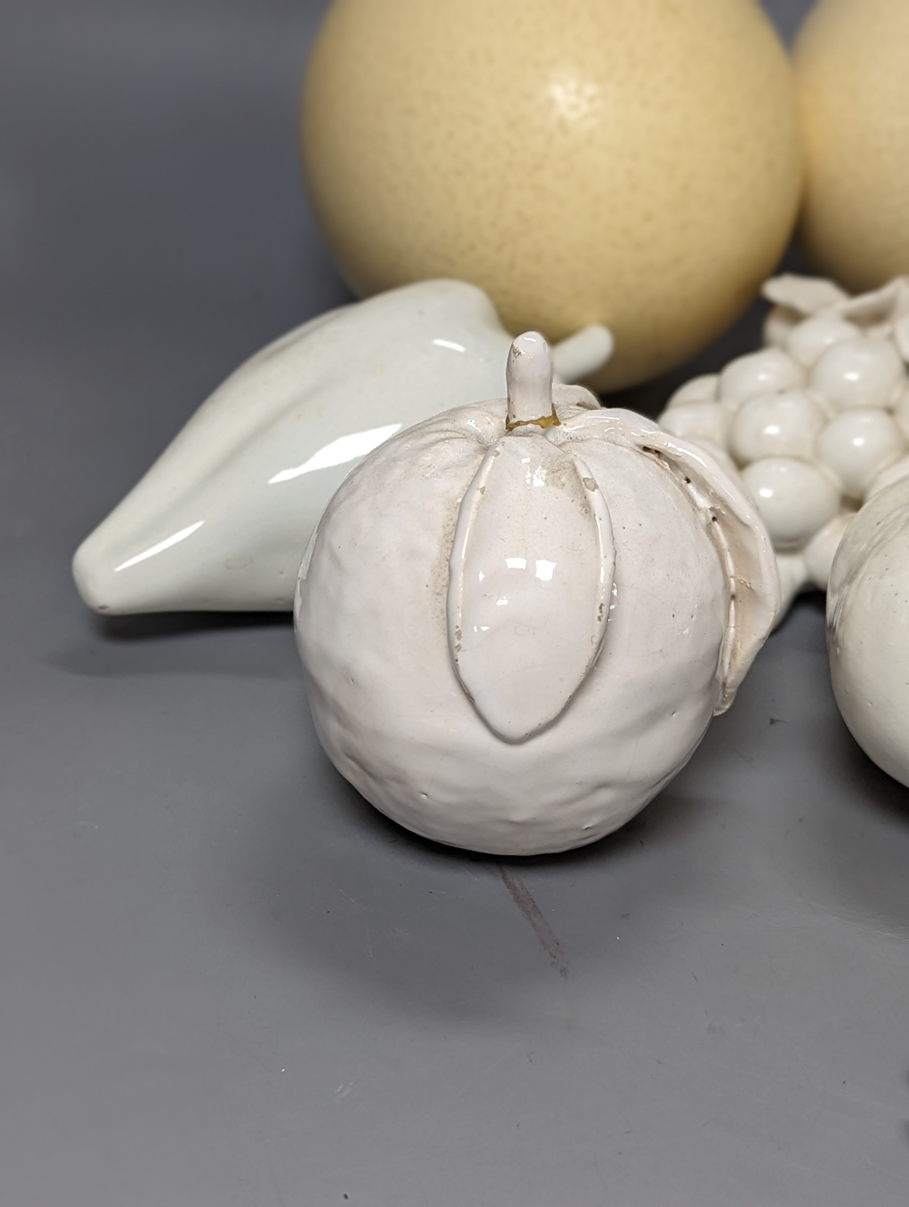 A decorative collection of tin glazed model fruits, together with three ostrich eggs